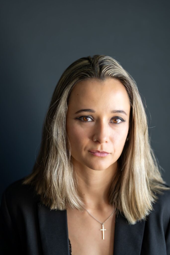 Portrait of Alisha Michaud, CEO of Michaud Foods, sitting confidently in a dark velvet armchair wearing a black blazer.